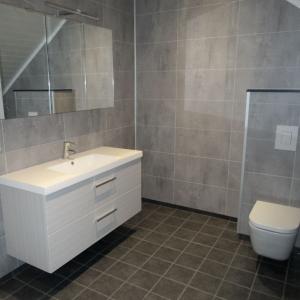 Ferdig baderom med flislagt gulv, Berry Alloc våtromsplater på vegg, vegghengt WC, vask og speil.