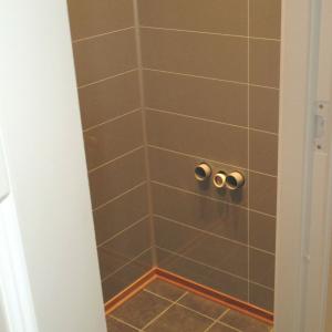 WC-rom: ferdig flislagt gulv og nye Berry-Alloc plater på vegger. Rør til servant stikker ut av veggen.