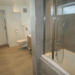 Ferdig baderom med badekar, dusjvegger, vegghengt WC, vask og speil. Fliser på gulv og enkelte vegger. Våtromsplater på andre vegger.